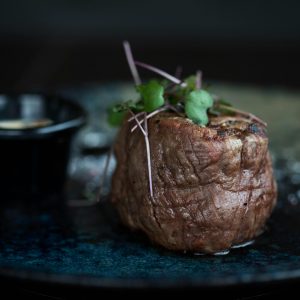 Succulent grilled steak topped with microgreens served on a dark plate for a gourmet meal.