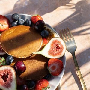 A mouthwatering stack of pancakes with figs, strawberries, blueberries, and cherries, perfect for brunch.